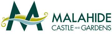 Logo for Malahide Castle and Gardens featuring two large, stylized dark green "M"s with a yellow and white decorative element resembling a medieval banner draped across them. The text "Malahide Castle and Gardens" is in dark green to the right of the emblem.