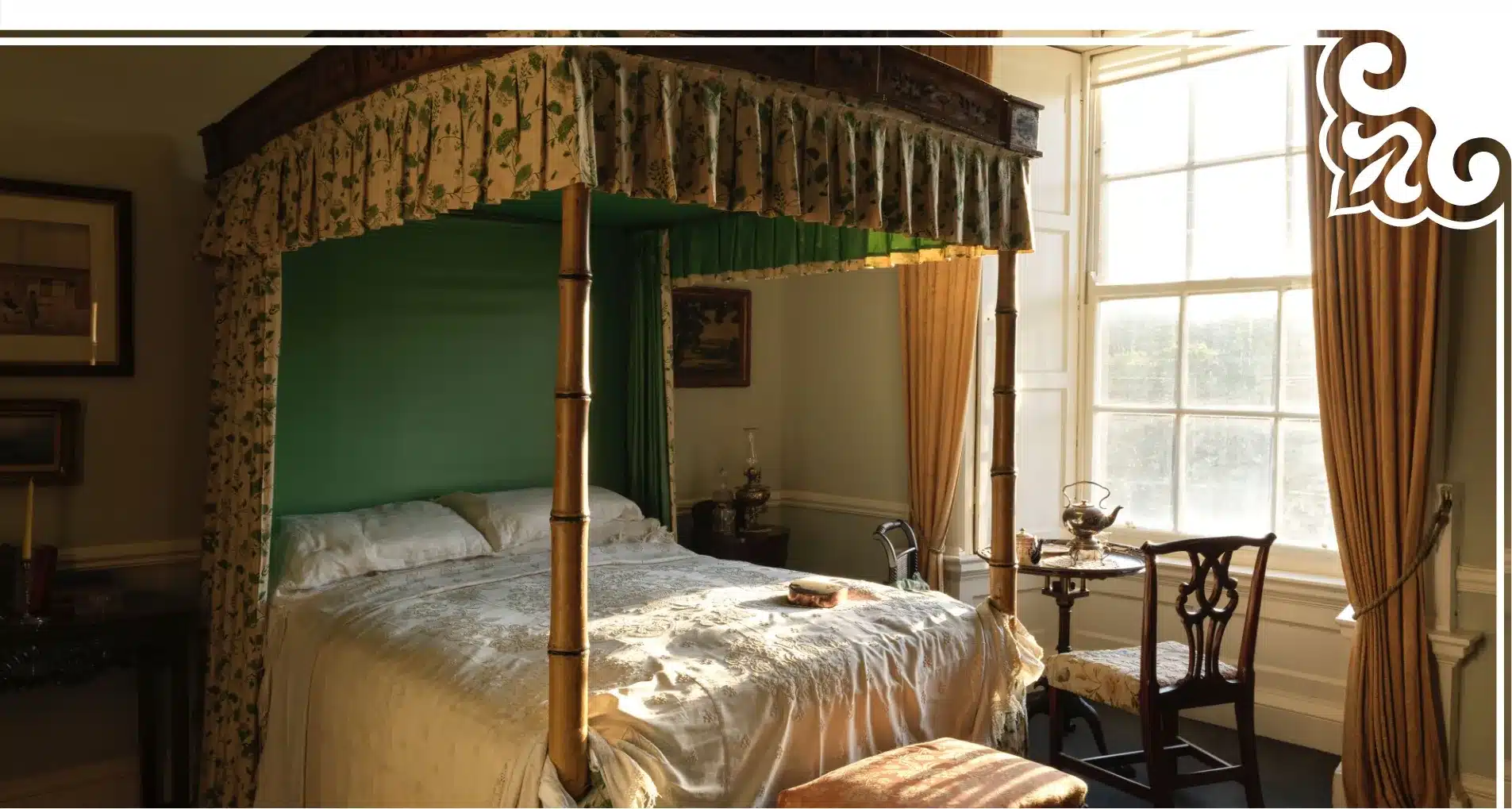 A vintage bedroom reminiscent of Malahide Castle, featuring a four-poster bed, green drapes, and floral patterns. Sunlight filters through a large window, illuminating a small table and chairs. Warm tones create a cozy, historical atmosphere.