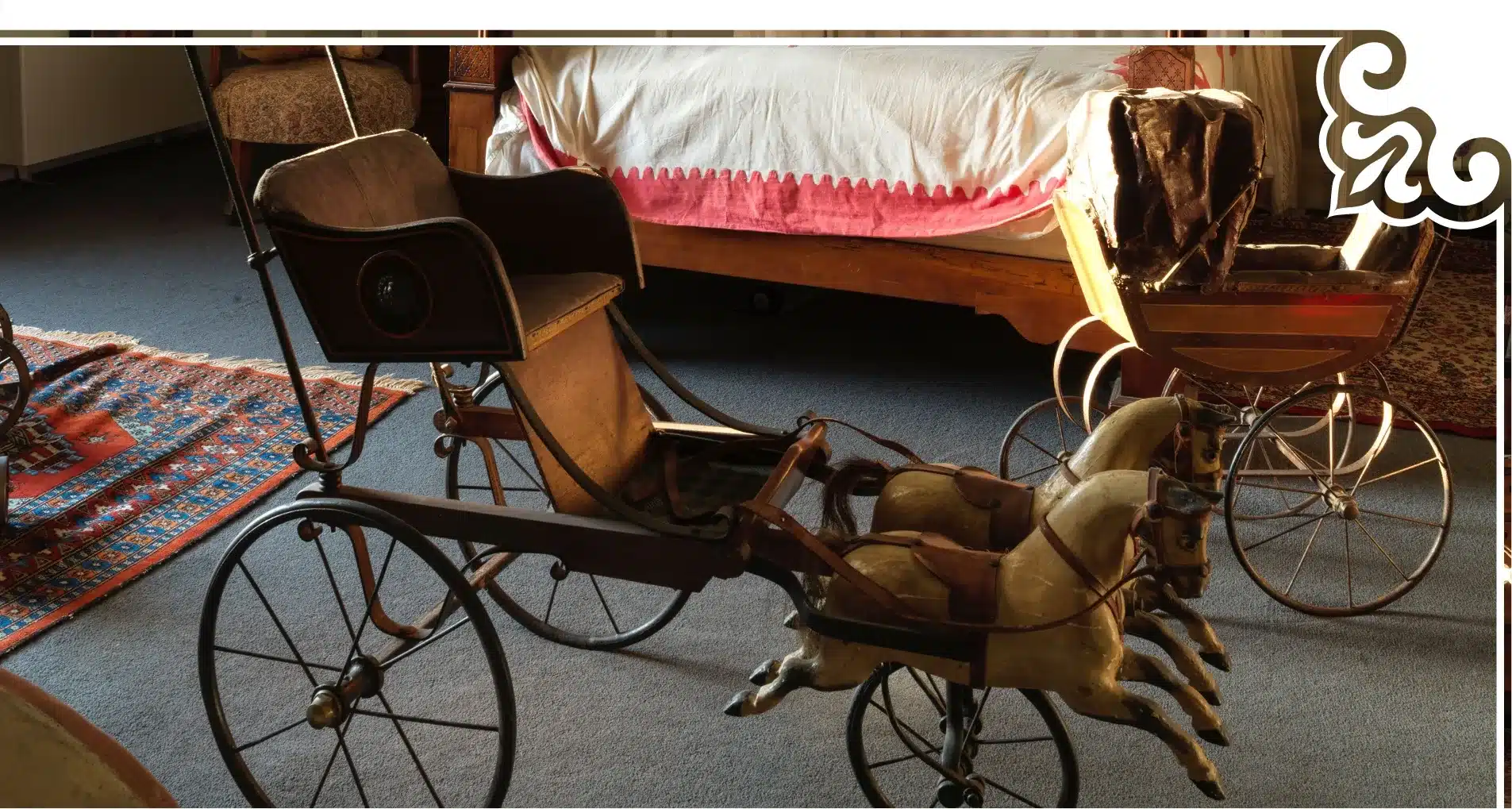 A vintage wooden toy carriage with two horse figures is displayed on a carpeted floor, reminiscent of treasures one might find at Malahide Castle. Behind it, a bed with a white and red coverlet is partially visible. Another smaller wooden toy rests in the background.