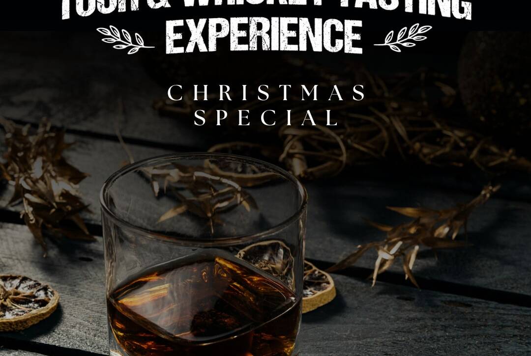 A glass of whiskey sits on a wooden table adorned with dried leaves and citrus slices. Bold white text above reads "Tour & Whiskey Tasting Experience" and "Christmas Special." The image has a dark, rustic ambiance.