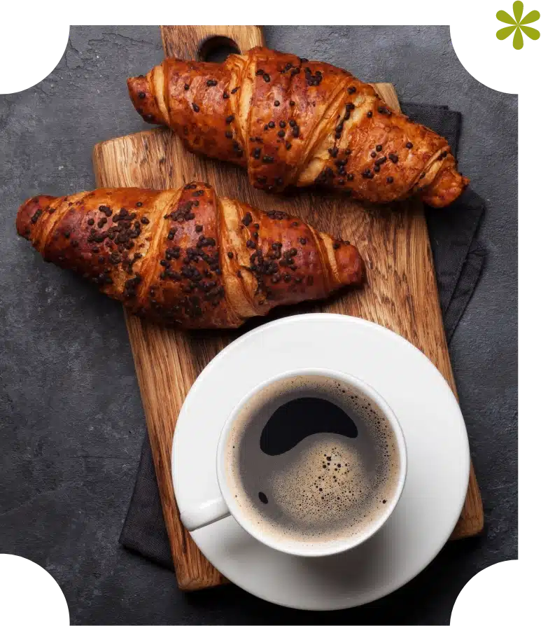 A top view of two chocolate croissants on a wooden cutting board evokes the charm of Malahide Castle. Nearby, a cup of black coffee invites you to indulge, all set against a dark textured surface.