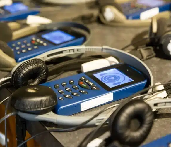 A group of blue audio guides with headsets sits on a table, ready for your Malahide Castle adventure. Each device features a digital screen displaying a heart symbol, with buttons and ports clearly visible. The focus is on the guide in the foreground, with others blurred in the background.