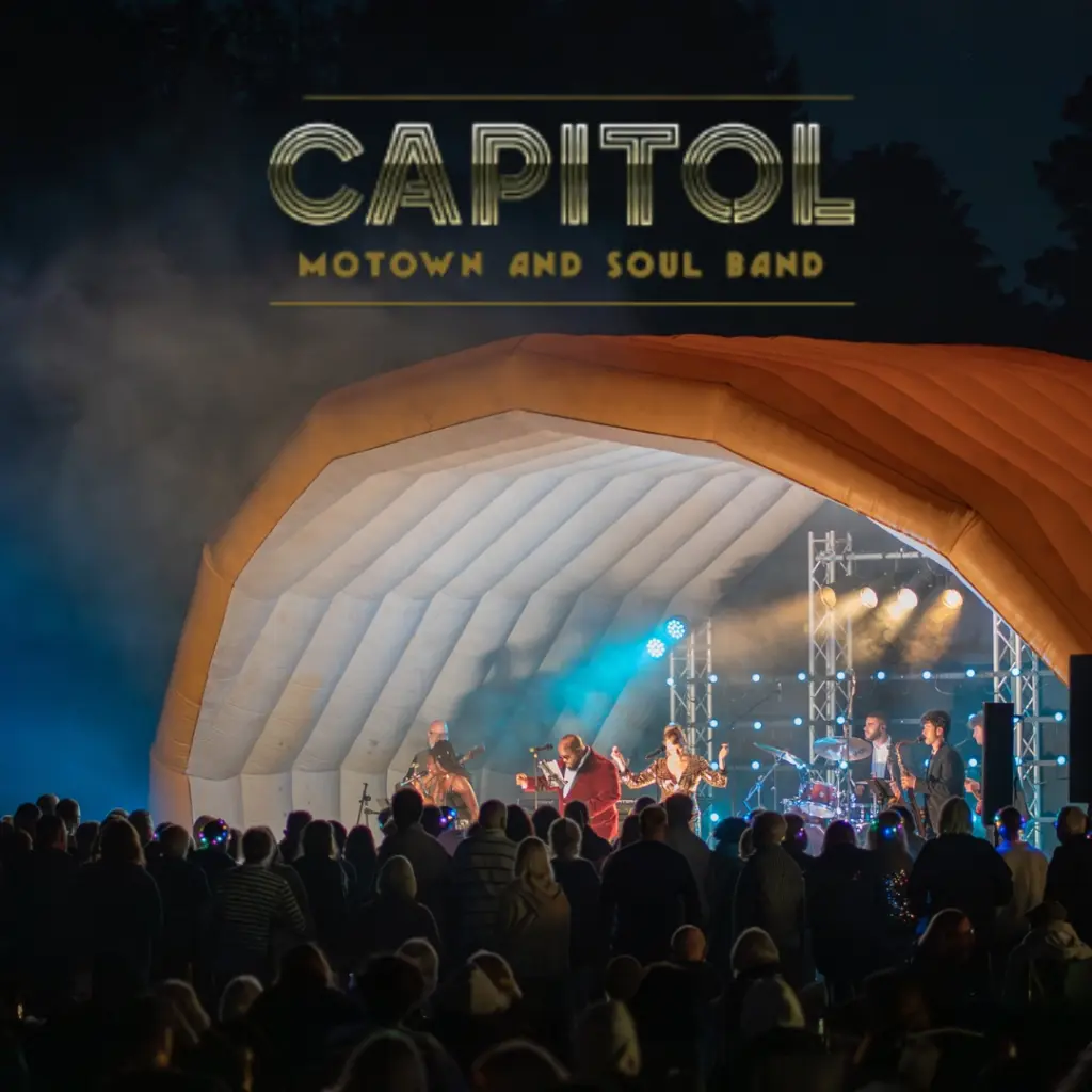 A Motown and soul band enchants the night as they perform under an inflatable shell canopy with "CAPITOL" shining above. While the tour offers soulful tunes, some enjoy a delightful whiskey tasting beneath the blue and purple stage lights.