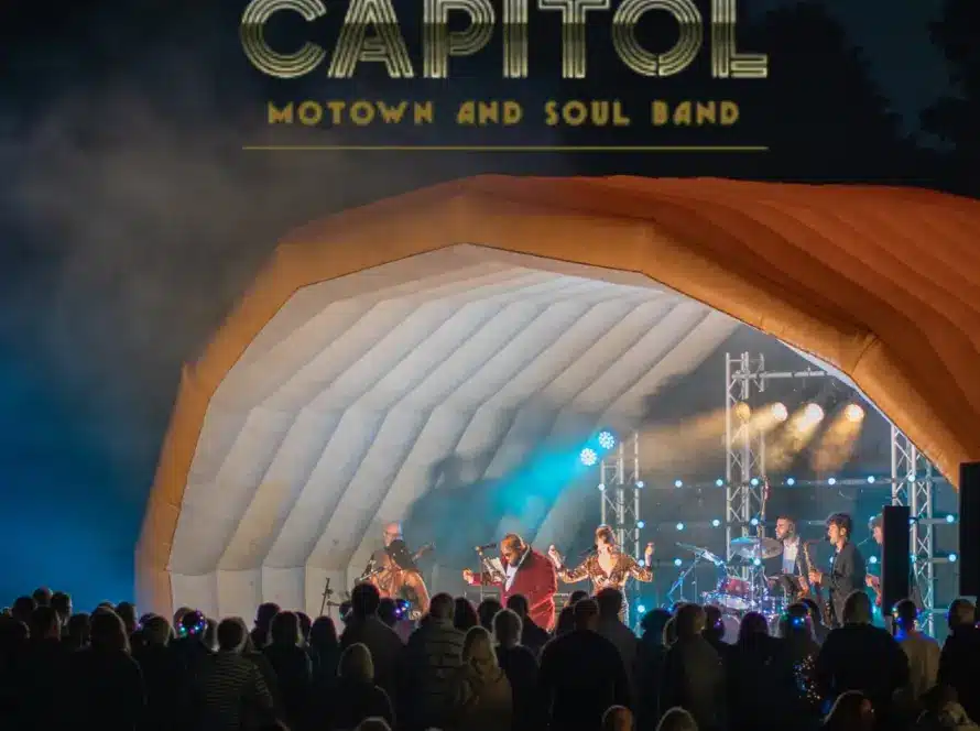 A Motown and soul band enchants the night as they perform under an inflatable shell canopy with "CAPITOL" shining above. While the tour offers soulful tunes, some enjoy a delightful whiskey tasting beneath the blue and purple stage lights.