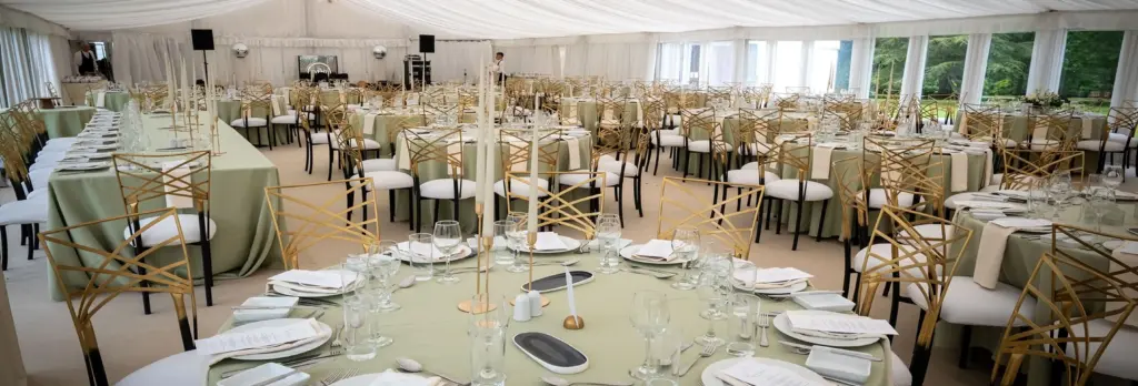 Elegant banquet hall with round tables set for an event, featuring light green tablecloths, gold chairs, and menus arranged neatly under a white draped ceiling—ideal for Private Hire Malahide Castle gatherings.