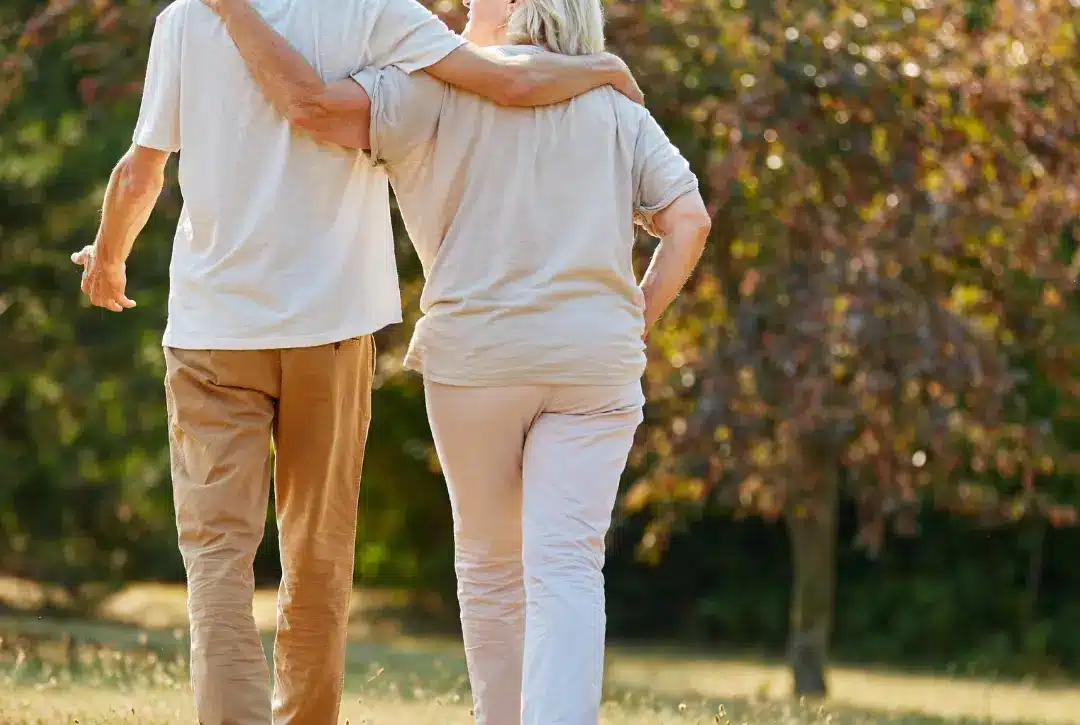 An elderly couple walks arm in arm through a sunlit park, dressed in light colors, with trees and grass in the background—capturing the kind of peaceful moment found at places like Malahide Castle, which belongs on your Ireland bucket list.