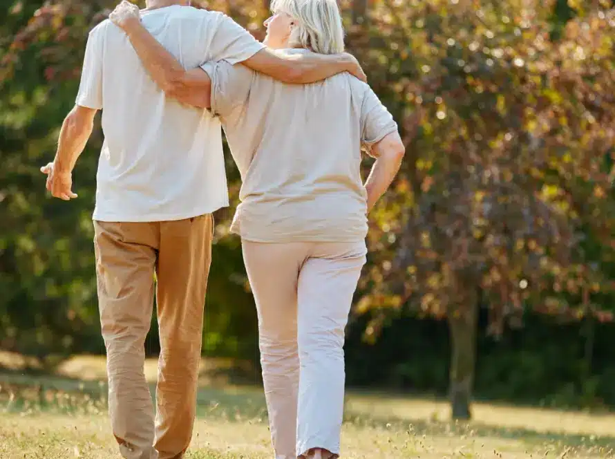 An elderly couple walks arm in arm through a sunlit park, dressed in light colors, with trees and grass in the background—capturing the kind of peaceful moment found at places like Malahide Castle, which belongs on your Ireland bucket list.