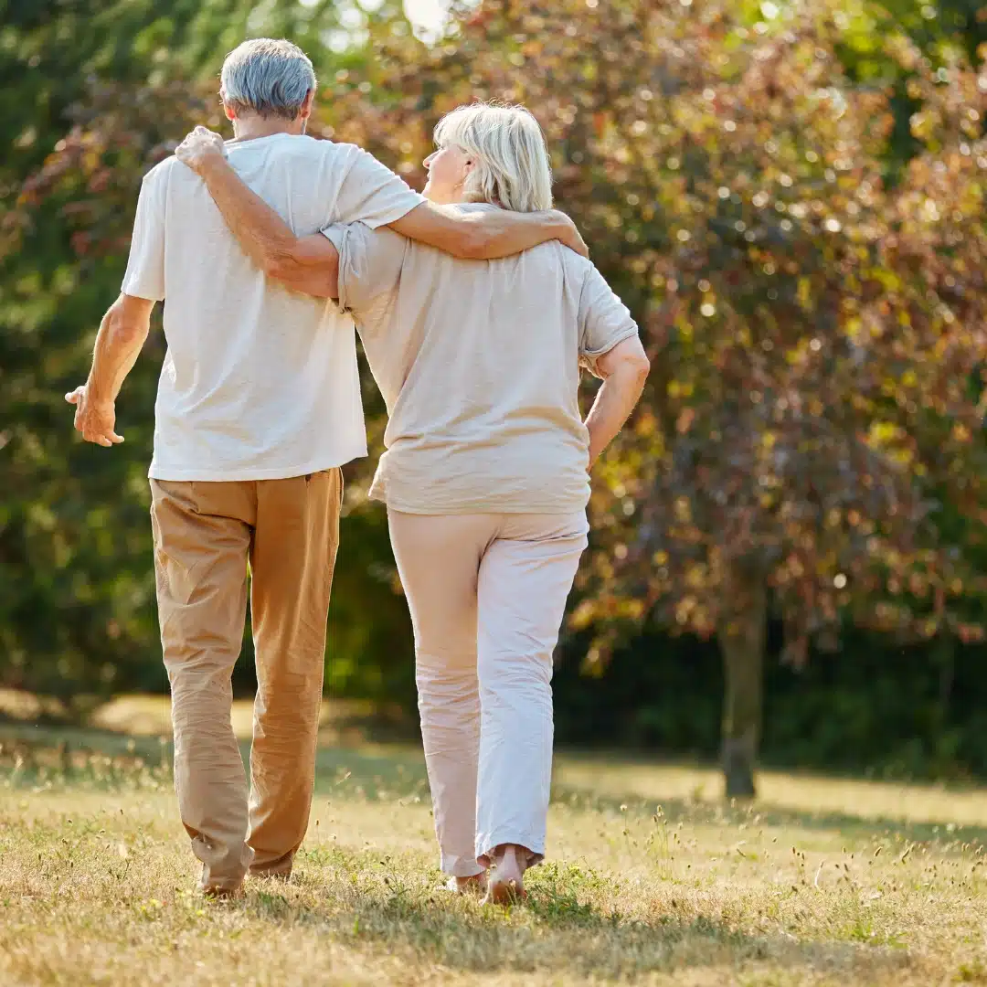 An elderly couple walks arm in arm through a sunlit park, dressed in light colors, with trees and grass in the background—capturing the kind of peaceful moment found at places like Malahide Castle, which belongs on your Ireland bucket list.