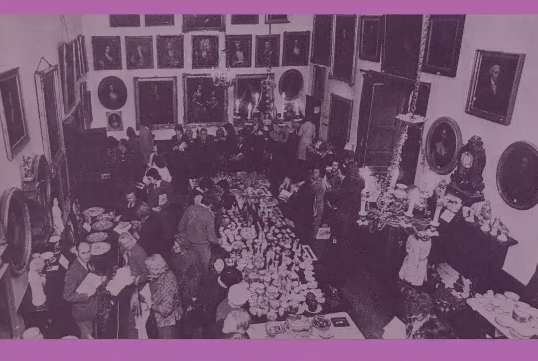 A sepia-toned photo of people at a large indoor gathering, surrounded by tables with various items and framed portraits. Text reads: “National Heritage Week - Upcoming Events at Malahide Castle & Gardens.”.