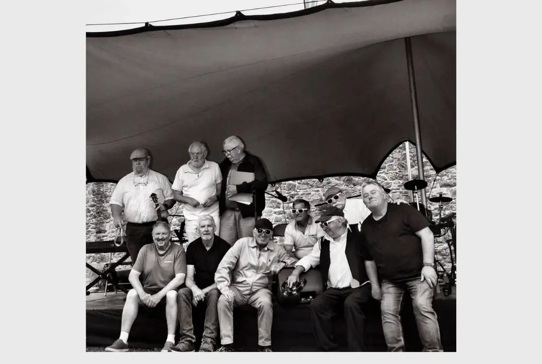 Black and white photo of ten men posing together on a stage under a canopy. Text above reads "The Courtyard Sessions" and below, "Gerry & The Plonkers."