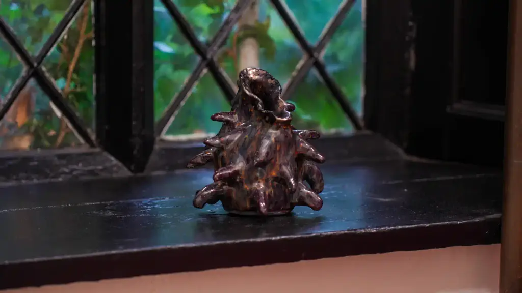 A dark, abstract, spiky sculpture sits on a black windowsill in front of a window with diamond-patterned glass, with greenery visible outside—a striking scene poised to capture attention during Culture Night 2025.