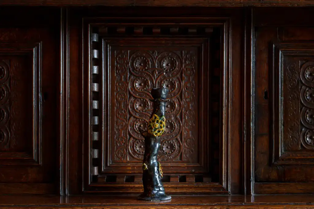 A small, dark figurine with yellow details stands in front of an ornate, carved wooden panel with intricate patterns, capturing the vibrant spirit of Culture Night 2025.