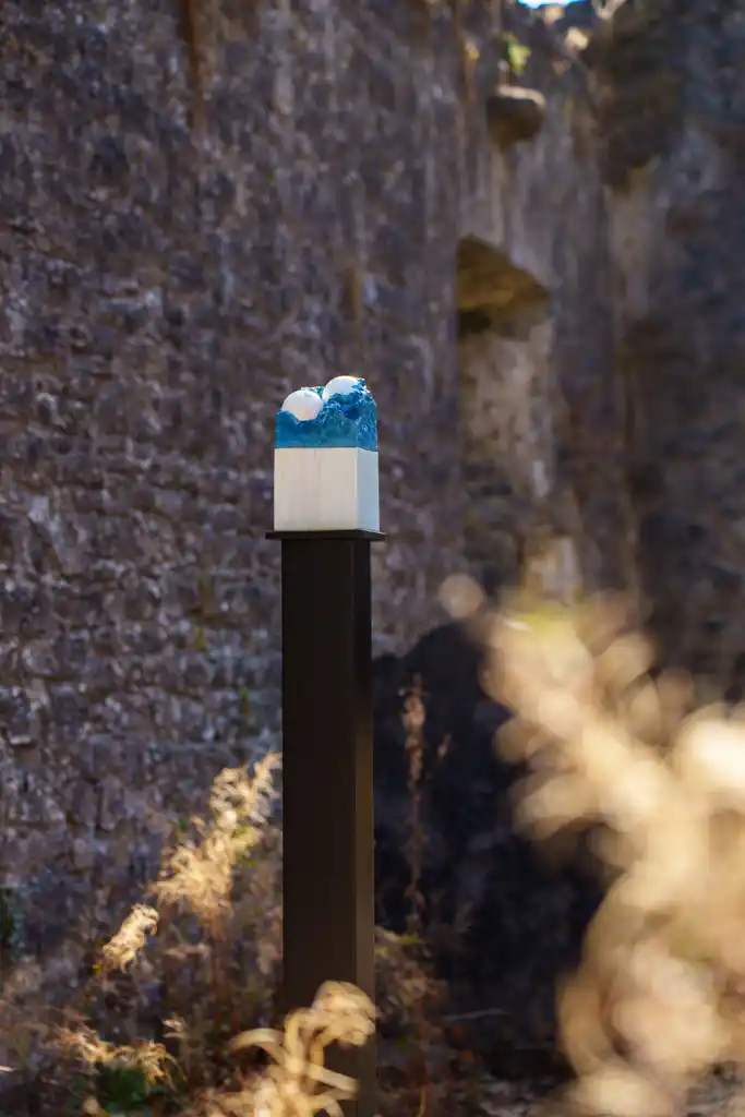 A small blue and white sculpture on a black plinth stands outdoors near an old stone wall, with sunlight and dry grass in the foreground—a striking display that captures the creative spirit of Culture Night 2025.