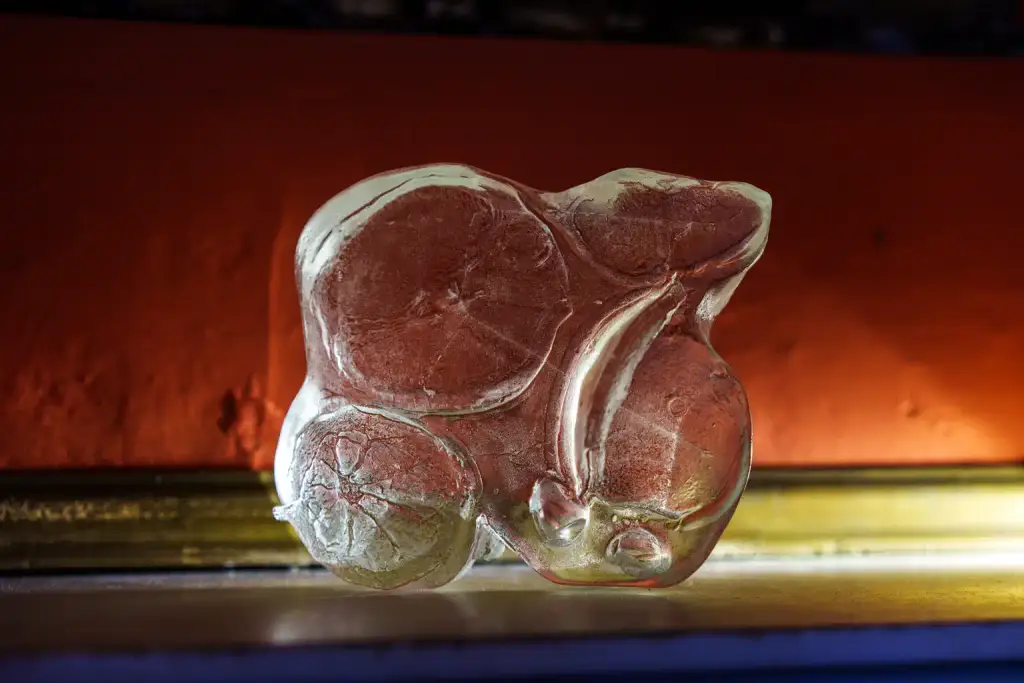 A translucent, abstract glass sculpture with red and white swirls sits on a surface, illuminated by the vibrant ambience of Culture Night 2025, with a blurred orange and yellow background accentuating its artistry.